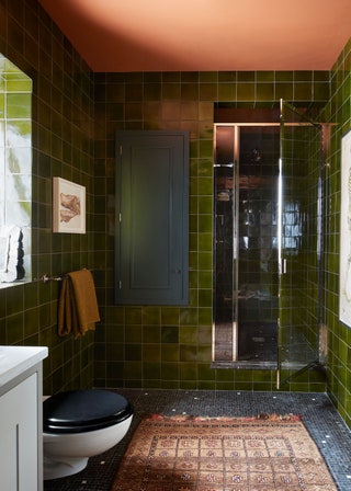 Bathroom lined with green tile walls coral ceiling gray and white mosaic floor beige patterned rug open shower stall