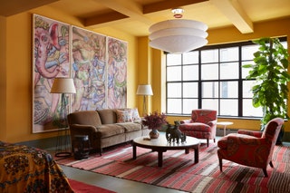 Guest suite sitting area with yellow walls framed triptych artwork on wall to left brown sofa two pink paisley patterned...