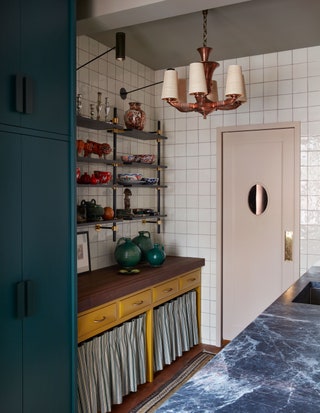 Marble countertops walls covered in white tiles hanging light fixture tall dark blue cabinetry open shelving with...