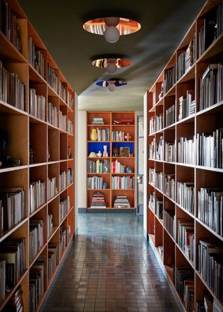 Narrow aisle lined with builtin bookshelves on both sides line of three light fixtures on ceiling bookshelf on far wall