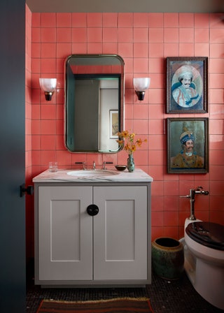 Pink tiled wall rectangular mirror flanked by two sconces above bathroom sink white cabinet two artworks on wall above...