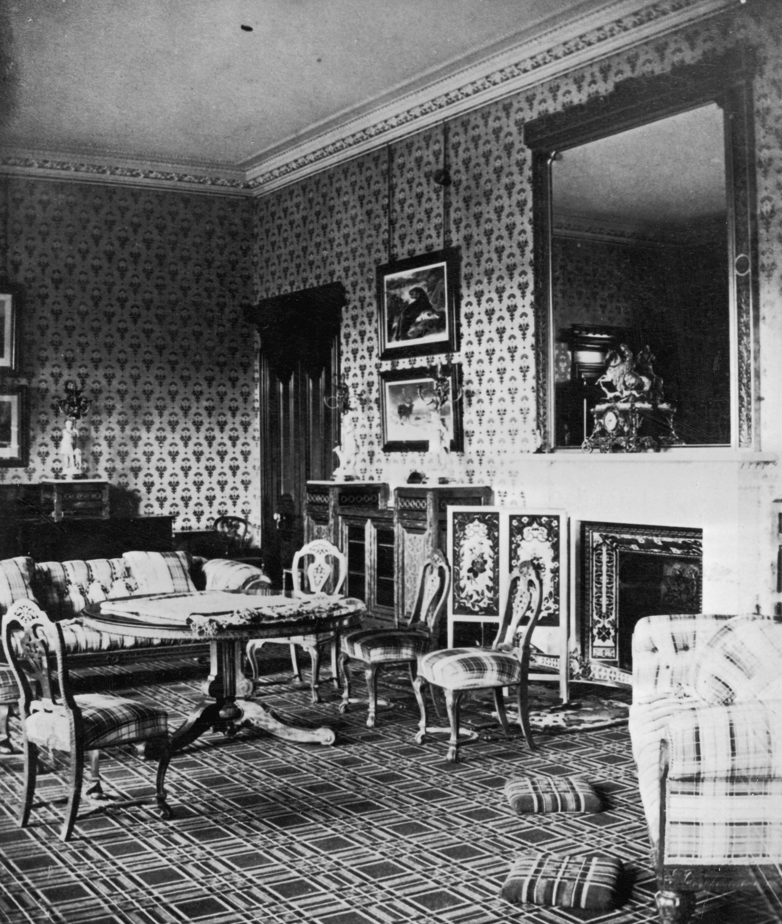 Living area in Balmoral Castle with patterned wallpaper fireplace chairs surrounding a round table sofa framed photos on...